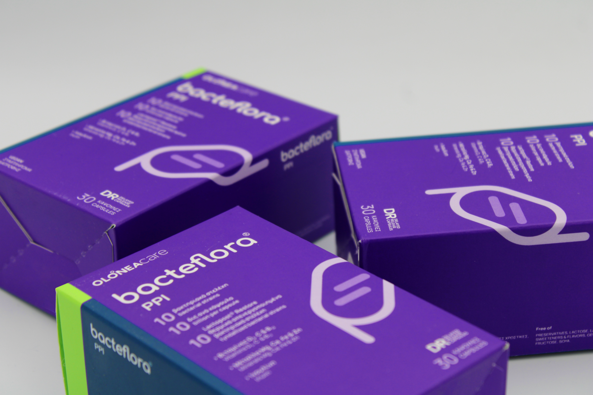 Purple boxes labeled with a probiotic product, stacked on a white surface with a bright green edge visible. Includes text indicating 30 capsules.