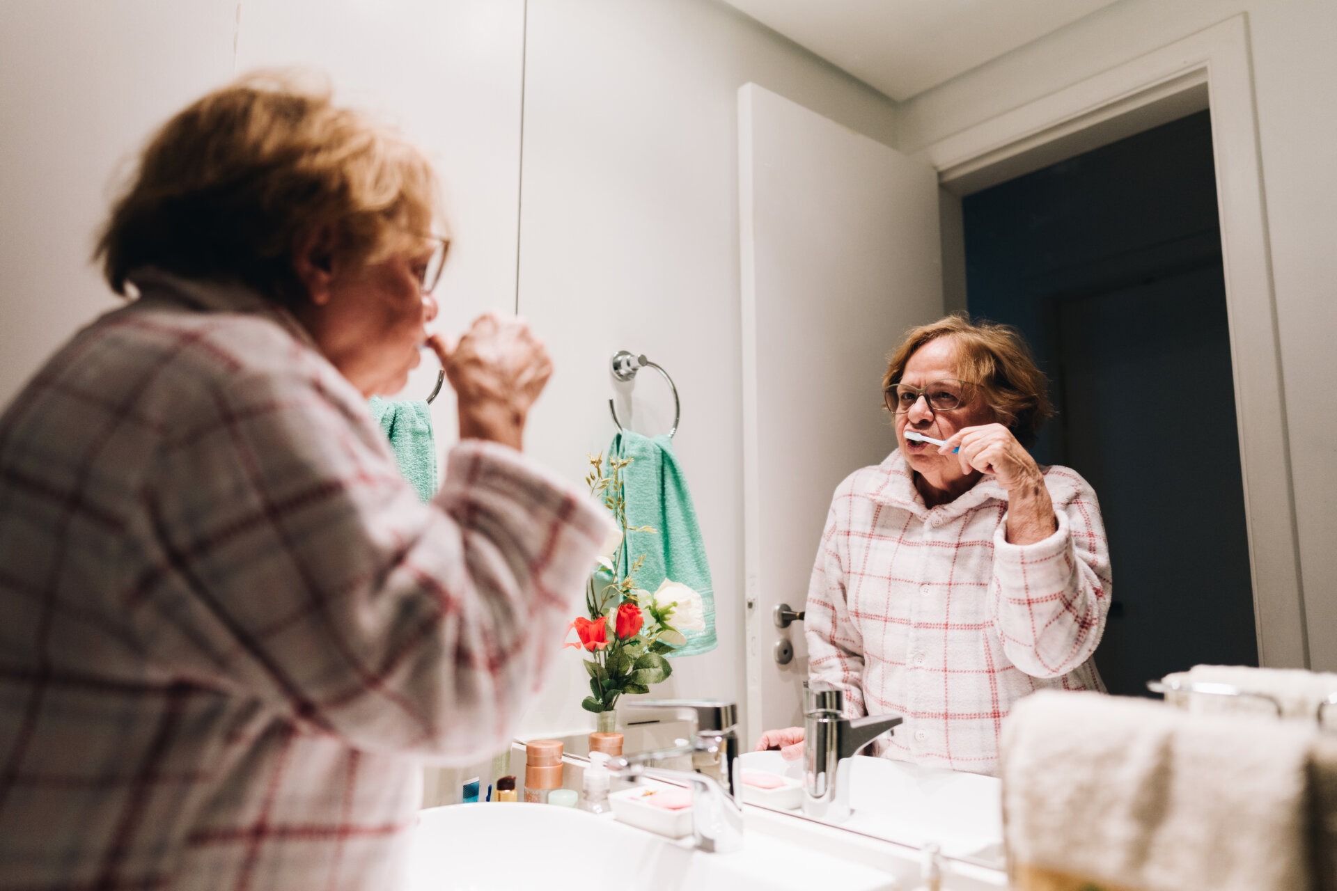 Μία κυρία μεγαλύτερης ηλικίας, στο μπάνιο του σπιτιού της, πλένει καλά τα δόντια της ώστε να θεραπευτεί από τη στοματίτιδα.