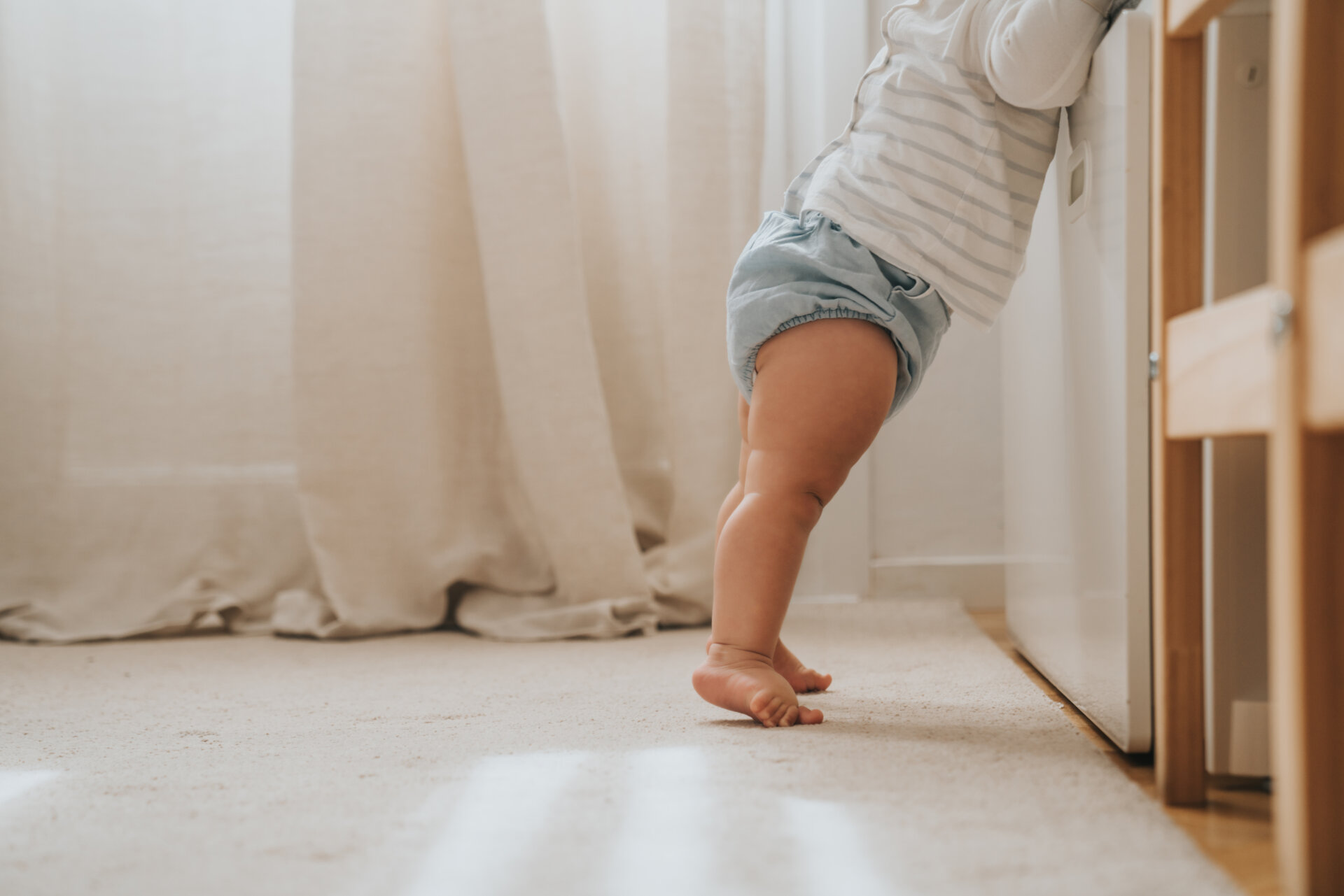 Κοντινό πλάνο στα πόδια ενός μωρού, που πιάνεται από το κρεβάτι του για να σηκωθεί από το πάτωμα.