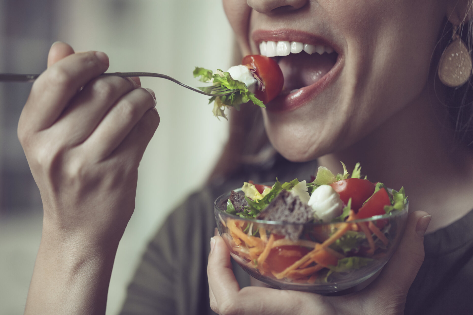 Κοντινό πλάνο μιας γυναίκας που τρώει μια σαλάτα με διάφορα λαχανικά εποχής, τα οποία είναι συχνά υπεύθυνα για την πρόκληση φουσκώματος.