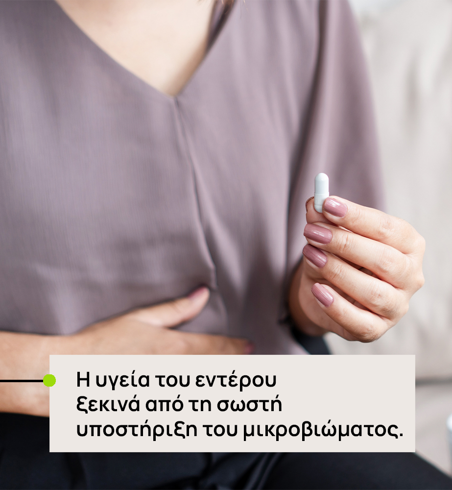 Person in a mauve top holds a small white capsule; overlay text in Greek about gut health and microbiome support: 'Η υγεία του εντέρου ξεκινά από τη σωστή υποστήριξη του μικροβιώματος.'