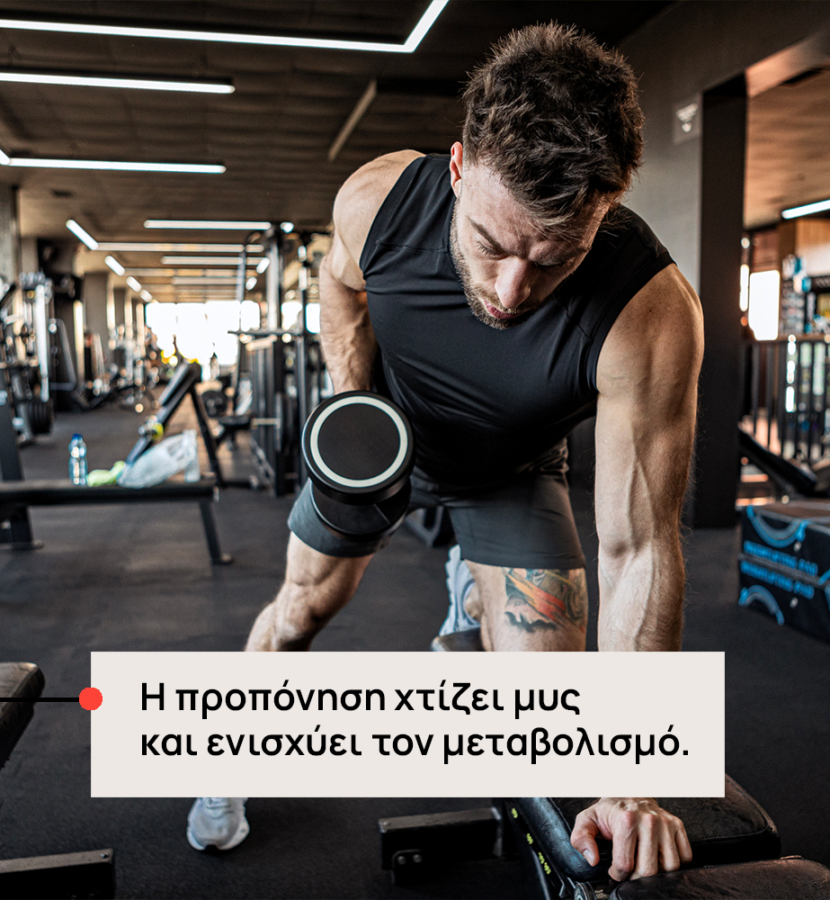 Man in a gym performing a bent-over dumbbell row; overlay Greek text reads: 'Η προπόνηση χτίζει μυς και ενισχύει τον μεταβολισμό'