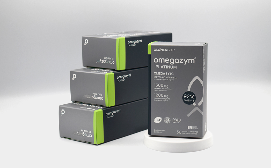 OmegaZym Platinum omega-3 supplement boxes in dark gray with lime green accents, arranged around a display box on a white pedestal.