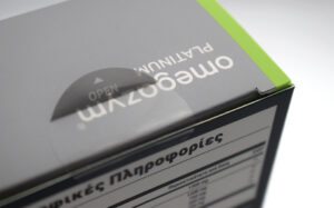 Close-up of a gray product box lid with a circular 'OPEN' dial and a bright green edge, revealing part of an information panel with Greek text.